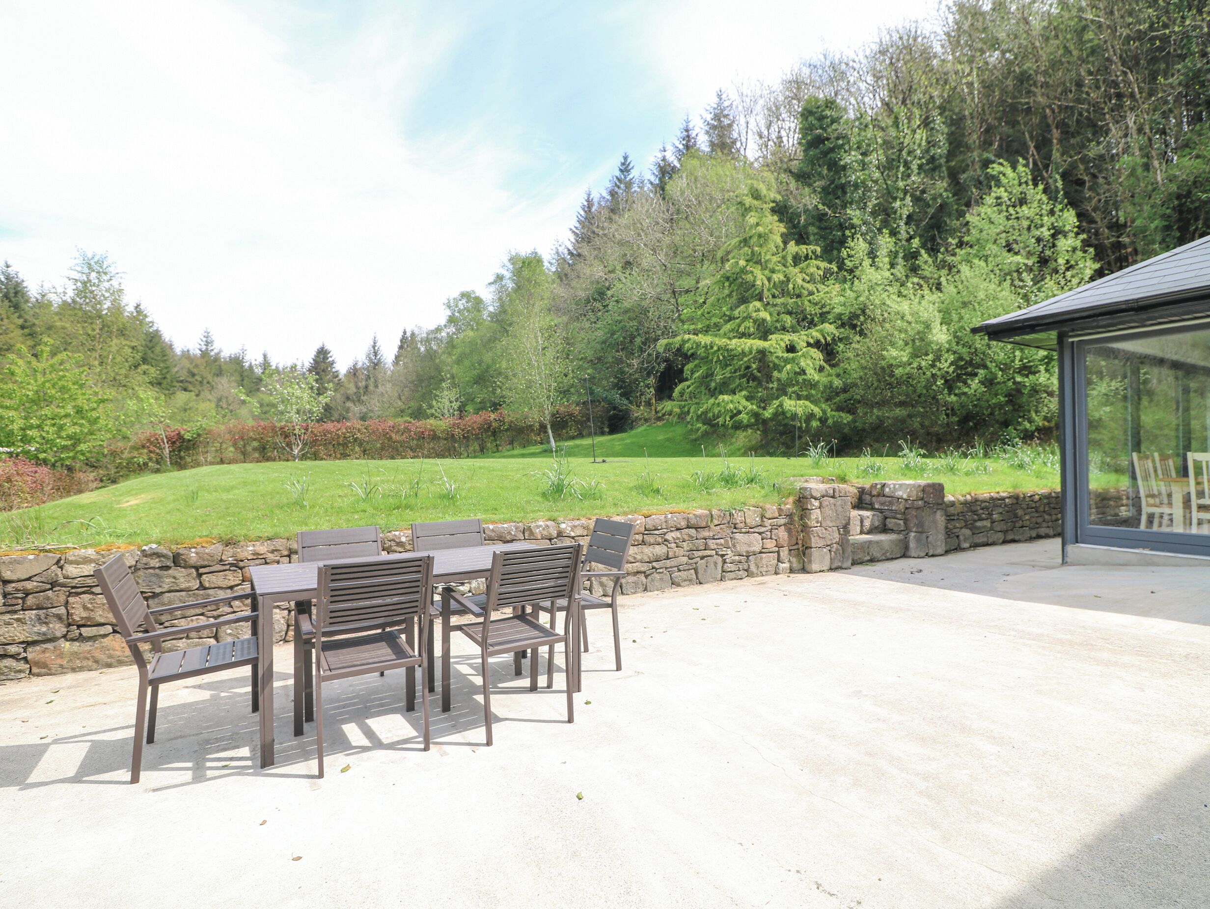 An outdoor patio with a stone wall, a table with chairs, and a glass enclosure.
