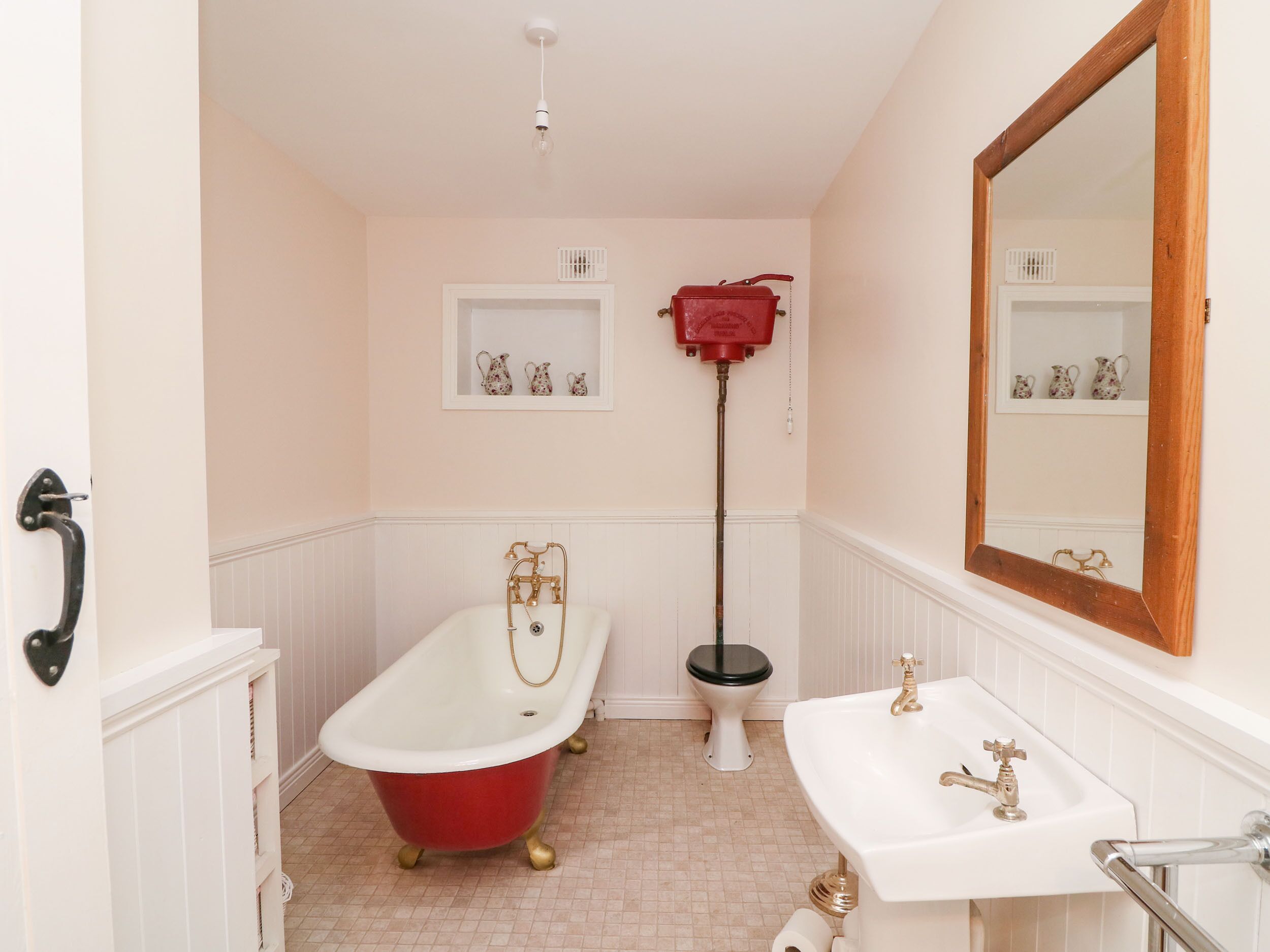 A bathroom with a red clawfoot bathtub, a white sink, a toilet, and a mirror.