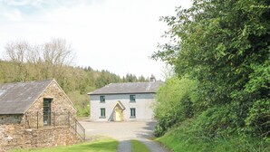 A stone cottage with a gravel path leading to a larger house with a stone facade and green windows.