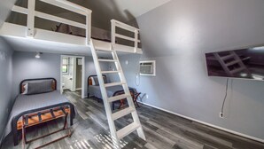 A room with bunk beds, a ladder, a TV, and a door leading to another room.