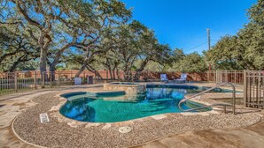 A swimming pool with a pebble-lined deck, surrounded by a fence and trees.