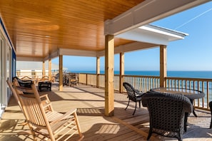 A wooden deck with outdoor furniture, a view of the ocean, and a clear sky.