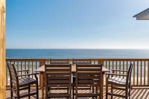 A wooden deck with a table and chairs overlooking the ocean.