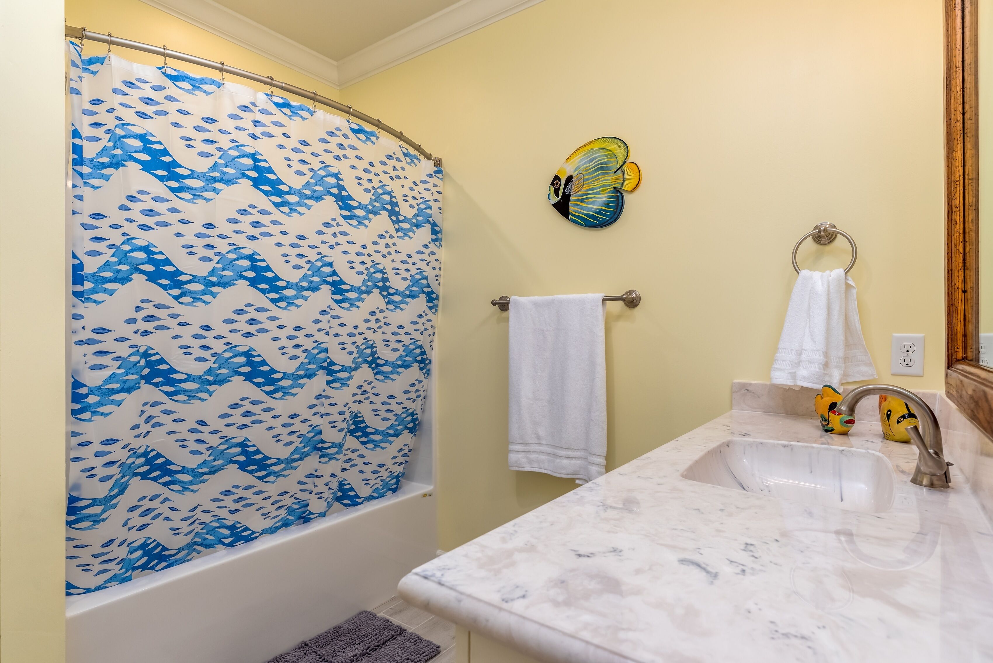 Um banheiro com cortina de chuveiro, pia, porta-toalhas e um detalhe decorativo de borboleta na parede.