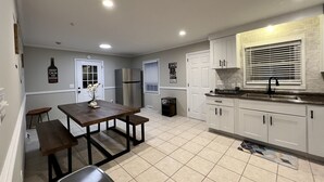 A modern kitchen with white cabinets, a stainless steel refrigerator, a dining table with benches, and a window with blinds. - 3 bedroom brick ranch (Apex)