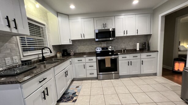 A modern kitchen with white cabinets, stainless steel appliances, and a tiled floor. - 3 bedroom brick ranch (Apex)