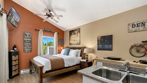 A bedroom with a wooden bed, a nightstand, a wall-mounted TV, and a window with curtains. - Industrial Old Town Bungalow W/ Free Cruiser Bikes (Fort Collins)