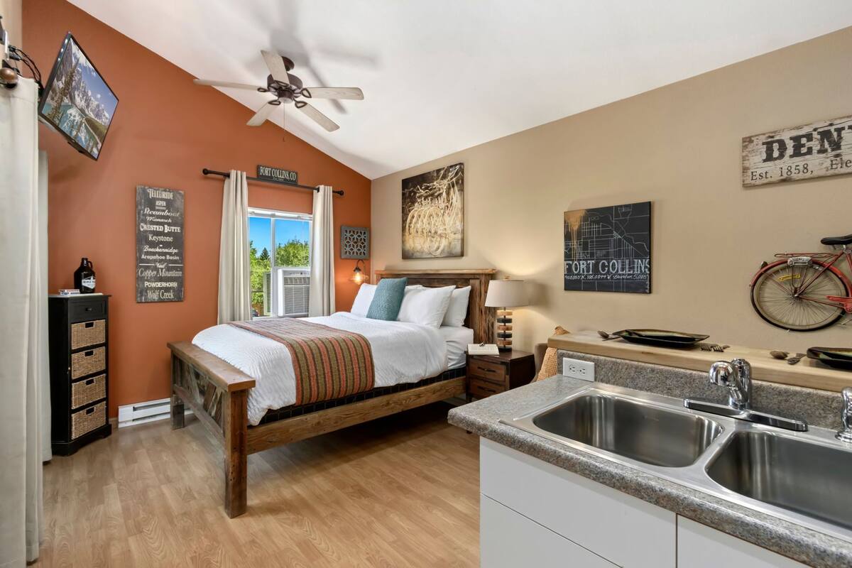 A bedroom with a wooden bed, a nightstand, a wall-mounted TV, and a window with curtains.