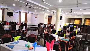 Un'ampia sala da pranzo con diversi tavoli, ventilatori a soffitto e un'area palco.