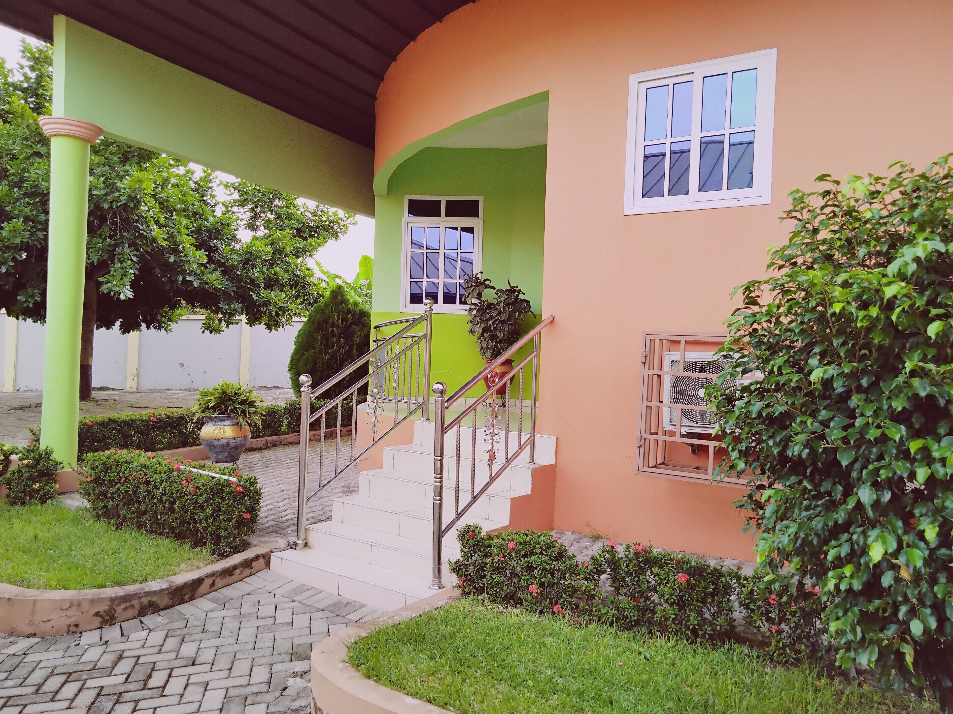 Un bâtiment à la façade verte et orange, un escalier avec des rampes en métal et une plante en pot près de l’entrée.