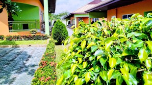 Un sentiero conduce a una fila di edifici dalle facciate verde e arancione, immersi nel verde curato e sotto un cielo sereno.