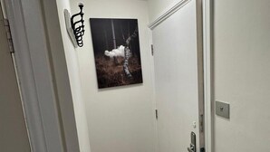 A hallway with a white door, a wall-mounted light fixture, and a framed picture of a tree. - Studio Sleeps 1 Near Acton Park (London)
