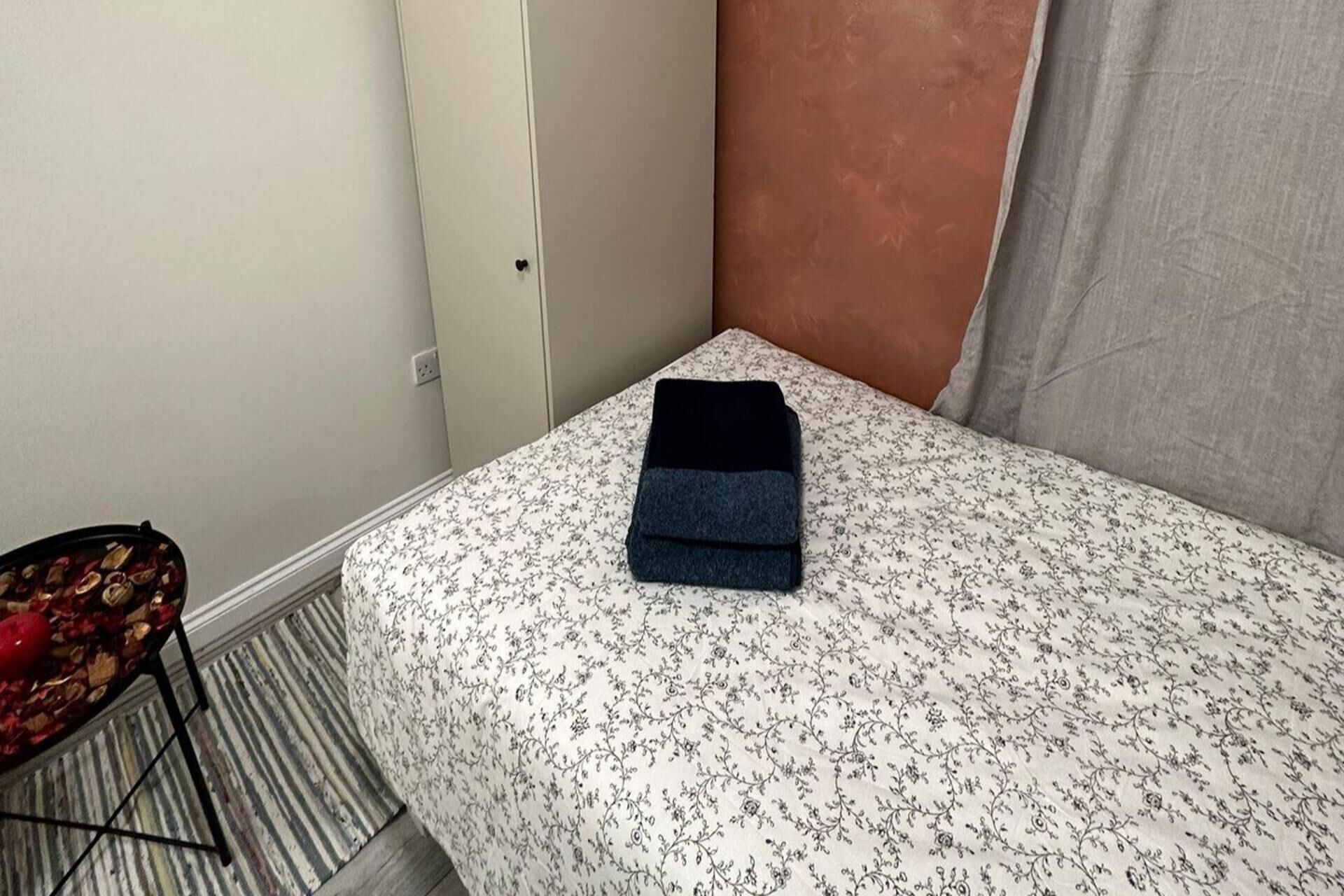 A small, neatly made bed with a floral bedspread and a folded dark blanket.