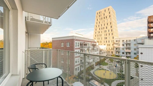 A balcony with a table and chairs, overlooking a courtyard with a playground and surrounding buildings. - Luxury Business Studio Apartment - Garden View (Sundbyberg)