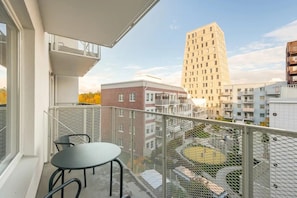 A balcony with a table and chairs, overlooking a courtyard with a playground and surrounding buildings.