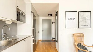 A modern kitchen with stainless steel appliances, a wooden floor, and a wicker chair. - Luxury Business Studio Apartment - Garden View (Sundbyberg)