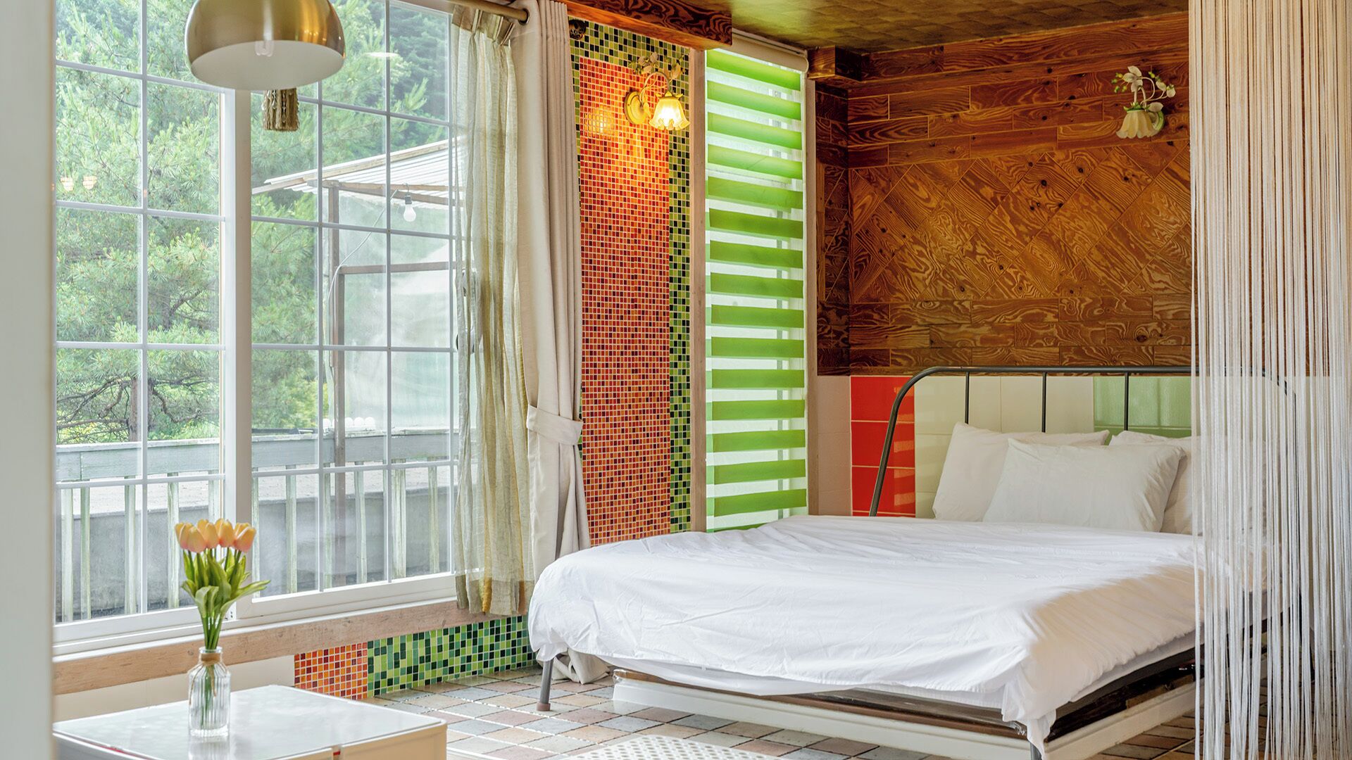 A bedroom with a bed, a window, a lamp, and a view of greenery outside.
