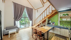 A modern kitchen with a wooden staircase, a dining area with a table and chairs, and a grey sofa. - Gapyeong Monami spa Pension (Gapyeong)
