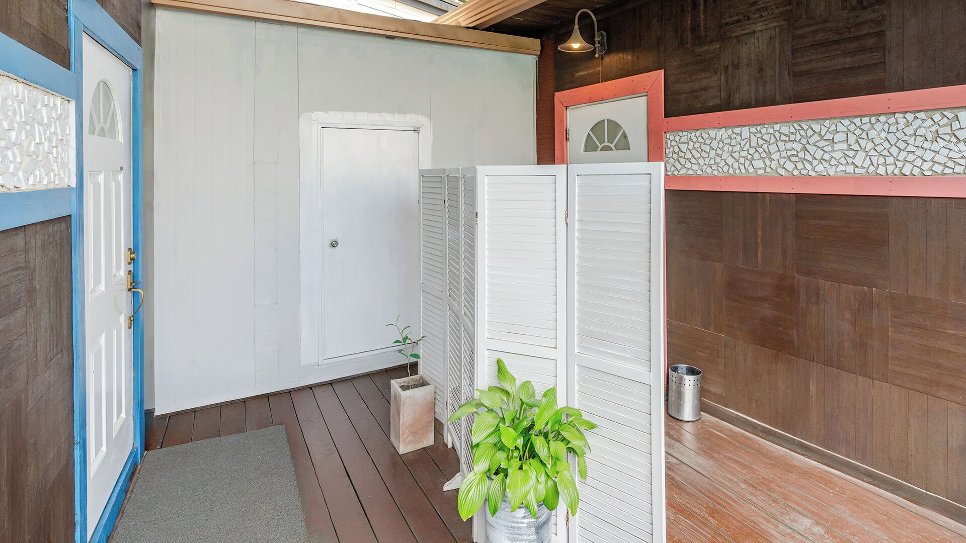 A wooden interior with a white door, a blue-framed door, a white partition, and a potted plant.