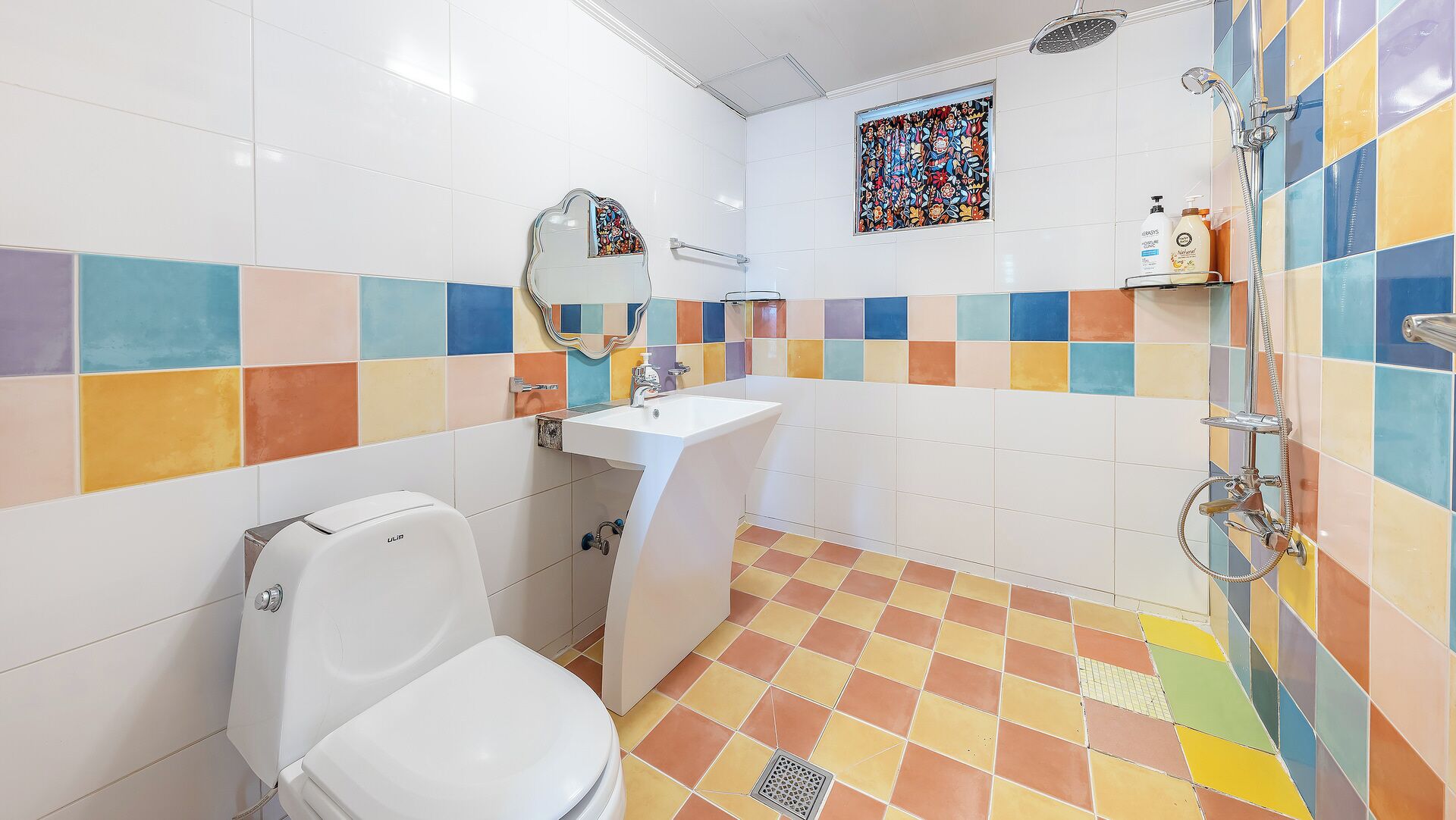 Un baño con inodoro, lavabo, ducha, azulejos coloridos y un vitral.