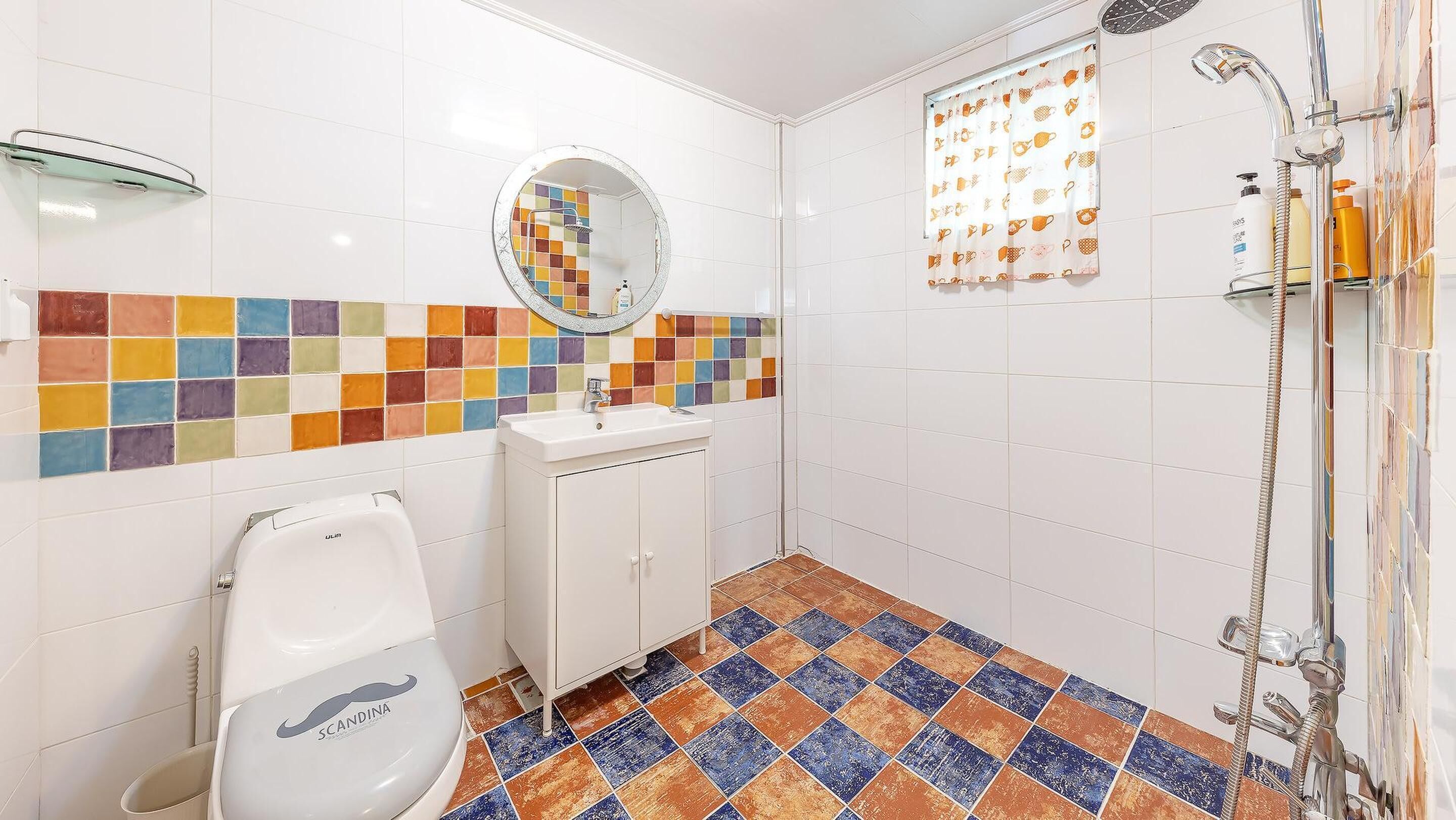 A bathroom with a toilet, sink, mirror, shower, and colorful tiled walls and floor.