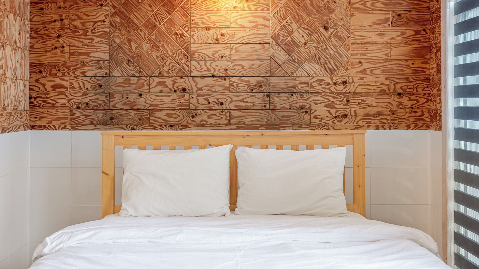 A bedroom with a wooden headboard, white bedding, and a patterned wall.