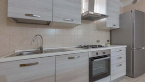 A modern kitchen with a stainless steel refrigerator, a built-in oven, a gas stove, and light-colored cabinetry. - 3151 Villa Giovì - Appartamento 4 by Barbarhouse (Manduria)