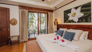 Quarto de hotel com uma cama grande, cabeceira de madeira, pintura de uma flor e vista para palmeiras pela porta de vidro.