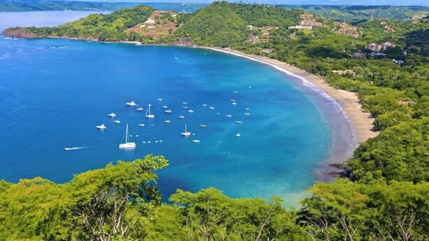 Paisagem costeira com praia, barcos e vegetação exuberante.