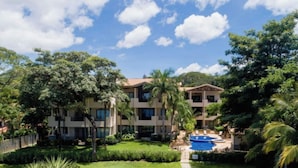 Um hotel com vários andares, um pátio central, piscina e vegetação exuberante.