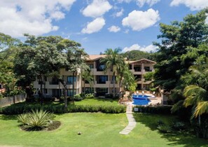 A multi-story hotel with a central courtyard, a swimming pool, and lush greenery. - Playa Hermosa Beachfront Condo • 3 BR • Ocean View • Resort Pool • Sol y Mar 3B (Playa Hermosa)