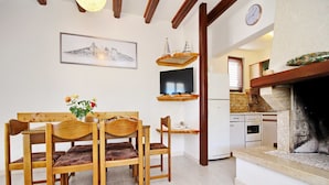 A dining area with wooden chairs and a table, a television on a wooden shelf, a kitchen with a stove, and a fireplace. - Oasis of Peace (Korcula)