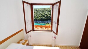 A room with a bed, a window with a view of a forest and a body of water, and a wooden floor. - Oasis of Peace (Korcula)