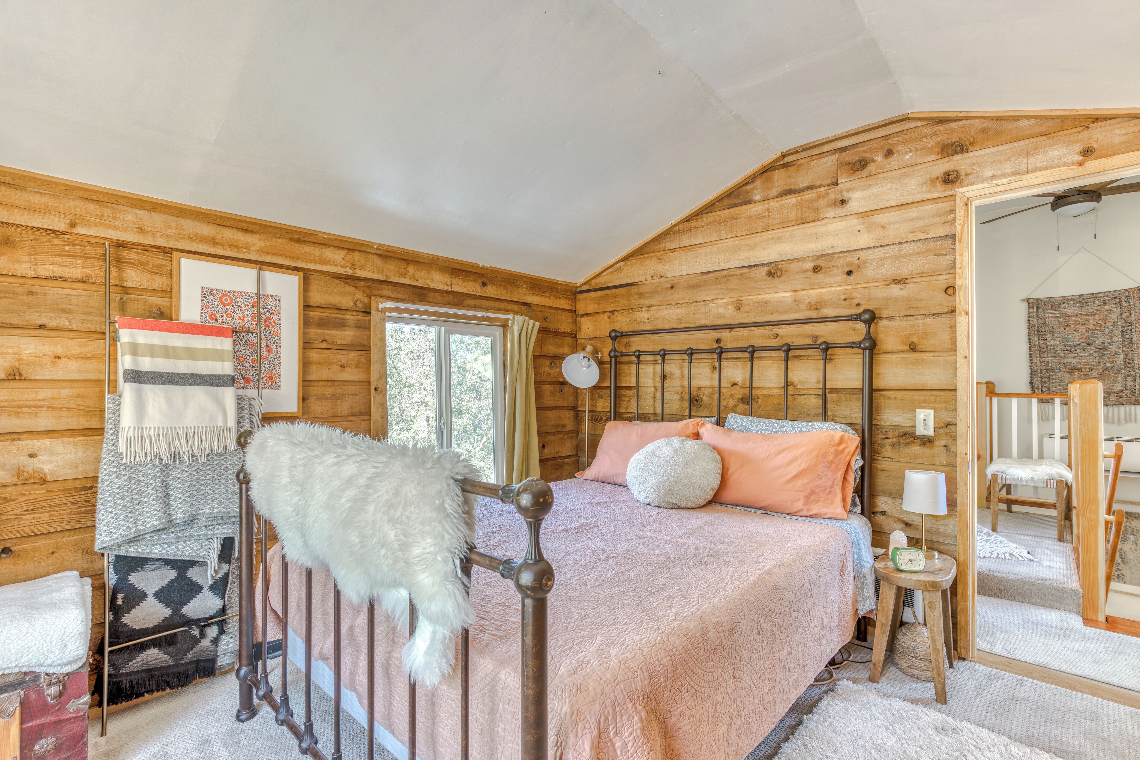 A wooden cabin bedroom with a bed, a mirror, and a window.