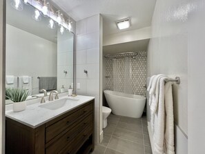 Un baño moderno con tocador doble, bañera independiente y cortina de ducha con diseño geométrico.