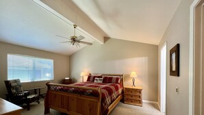 Ein Schlafzimmer mit einem hölzernen Bett, einem Schreibtisch, einem Stuhl, einem Deckenventilator und einem Fenster mit Jalousien.