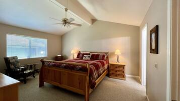 A bedroom with a wooden bed, a desk, a chair, a ceiling fan, and a window with blinds.