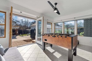 A modern room with a foosball table, large windows, and a ceiling fan.