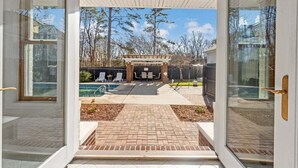 A view through a glass door into a backyard with a patio, a pool, and a barbecue area. - NEW! minutes to downtown - Private Half-Acre Ranch Retreat (Charlotte)