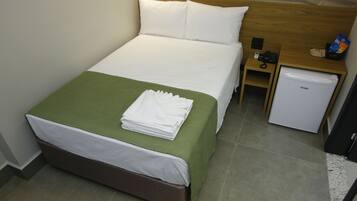 A hotel room with a bed, a nightstand, a small refrigerator, and a green bedspread.