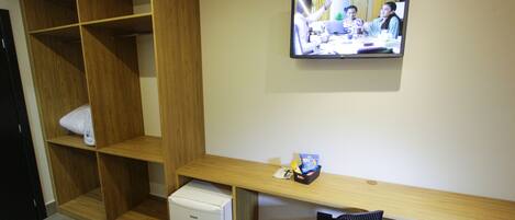 Habitación de hotel con armario de madera, un refrigerador blanco pequeño, un escritorio de madera con una silla y un televisor fijado a la pared.