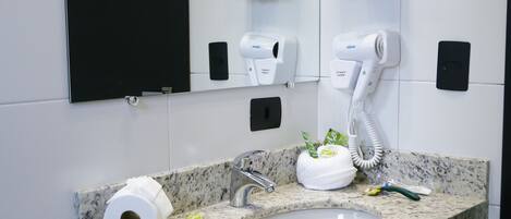 Un baño con lavamanos de encimera de granito, dos toallas blancas, un secador de pelo y un espejo.
