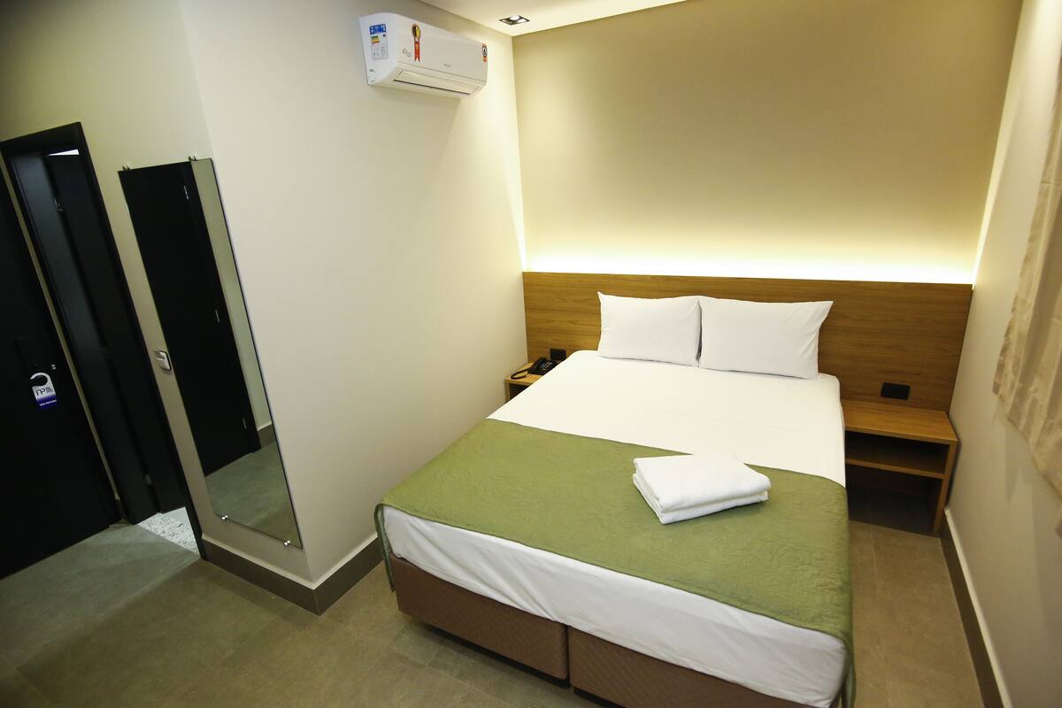 A hotel room with a bed, bedside table, and a mirror.