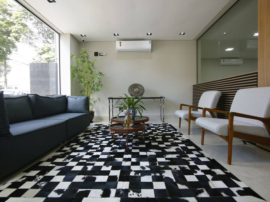 A modern waiting area with a black and white checkered floor, a sofa, two chairs, a small table with a plant, and an air conditioning unit on the wall.