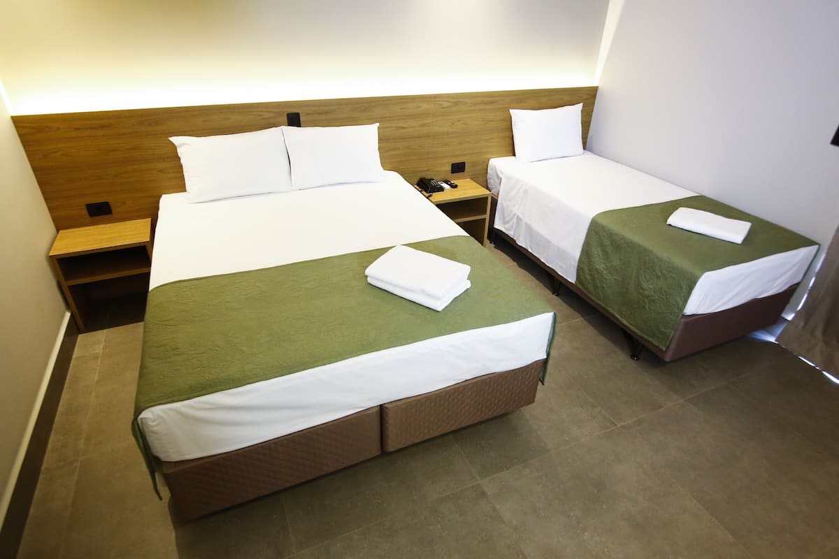 A hotel room with two single beds, each with a green bedspread and white linens, and a wooden headboard.