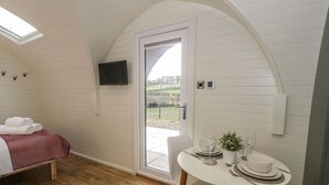 Une pièce confortable comprenant un lit, une table à manger avec des chaises, un téléviseur fixé au mur et une porte donnant sur un espace extérieur.