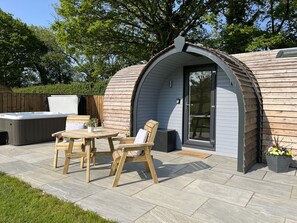 A cozy outdoor seating area with a wooden table and chairs, a hot tub, and a covered patio. - Yr Onnen (Ruthin)