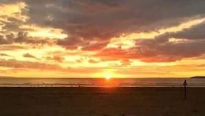 Una playa al atardecer con una persona caminando sobre la arena.