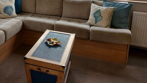 Una sala de estar acogedora con un sofá seccional, una mesa de centro de madera y vistas a una zona residencial con casas y un coche estacionado.