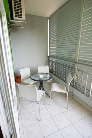 Ein kleiner Balkon mit rundem Tisch und vier Stühlen, ein Fenster mit Jalousien und einem Metallgeländer.